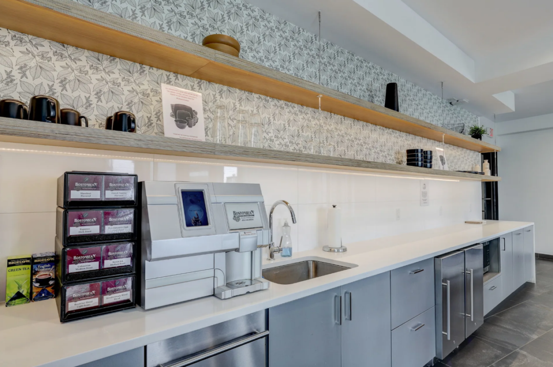 Shared kitchenette with a coffee machine, sink, open shelves, and undercounter appliances.