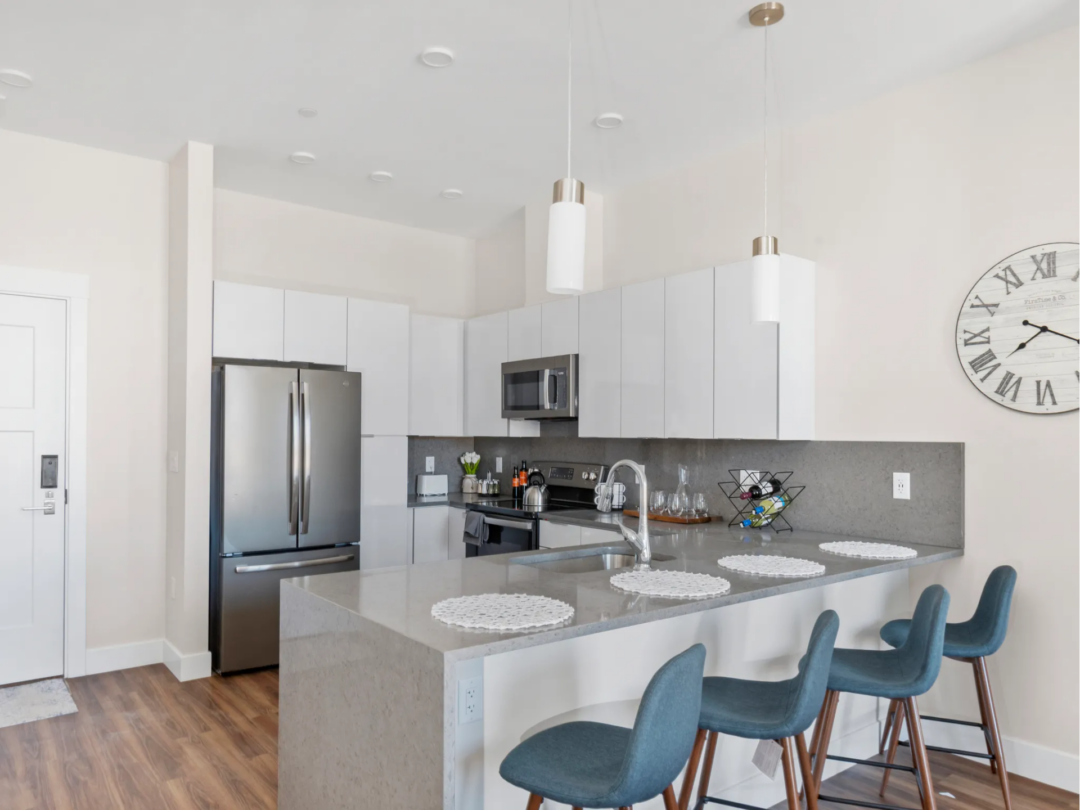 Bright kitchen with white cabinets, stainless steel appliances, and a gray island with blue upholstered stools.