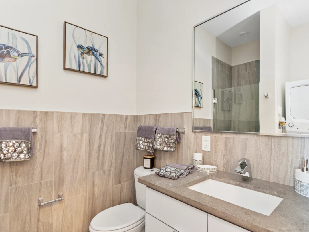 Bathroom with a white vanity, beige countertop, large mirror, toilet, and wood-look wall panels.