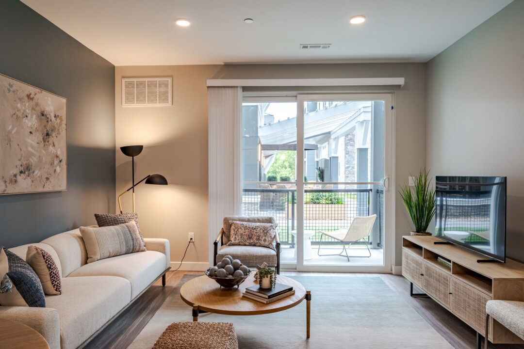 Living room with a gray sofa, round coffee table, floor lamp, and sliding glass doors opening to a balcony.