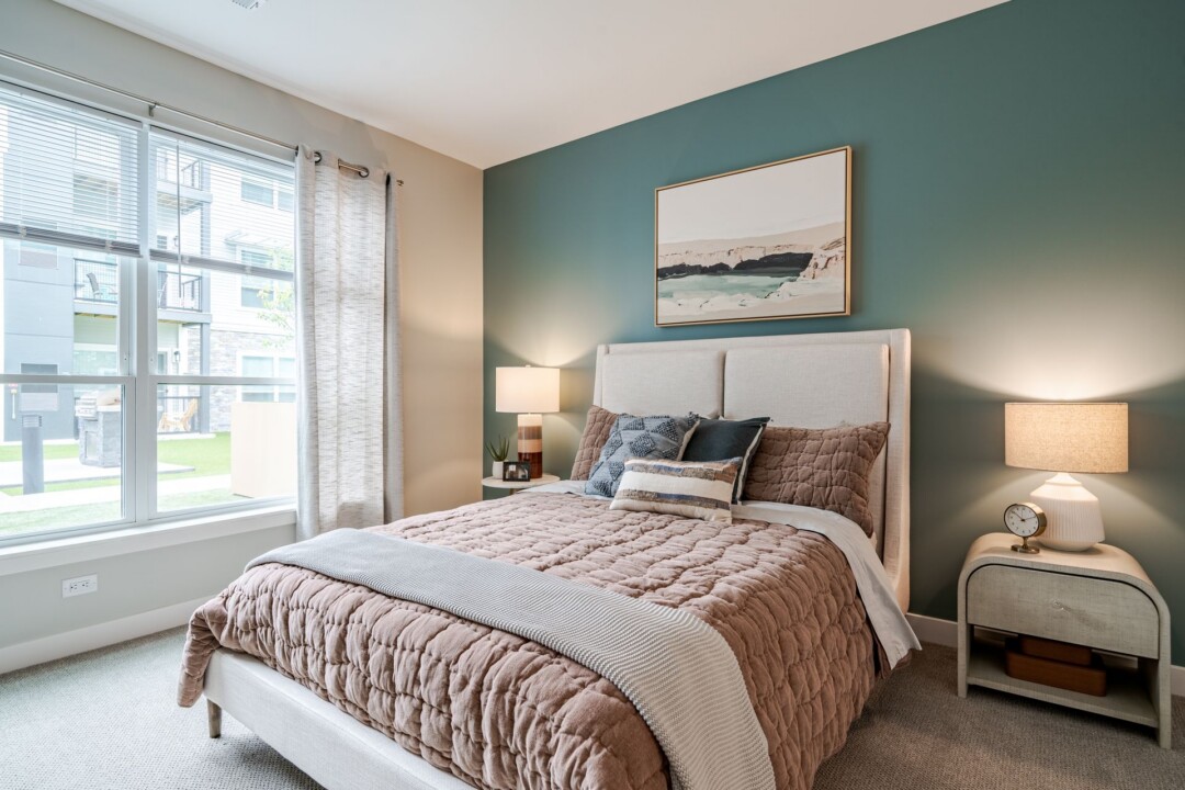 Furnished bedroom with a teal accent wall, upholstered bed, bedside lamps, and framed artwork above the headboard.