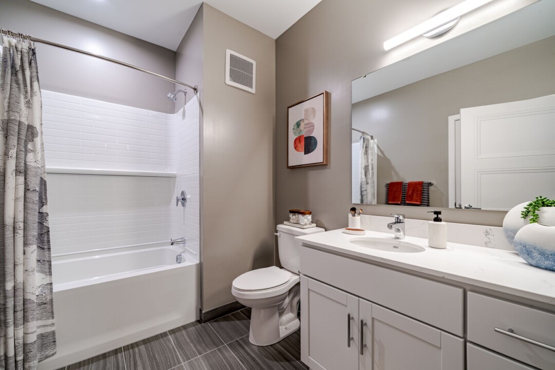 Bathroom with a bathtub and shower curtain, toilet, and white vanity beneath a large mirror.