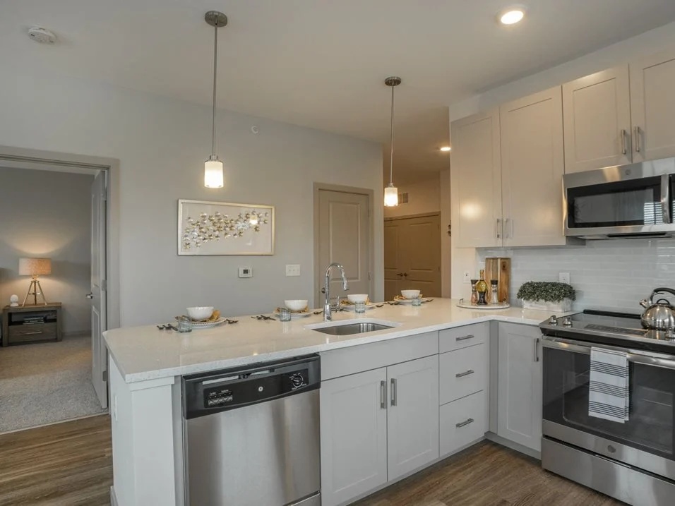 Kitchen with white cabinets, stainless steel dishwasher, and island seating.