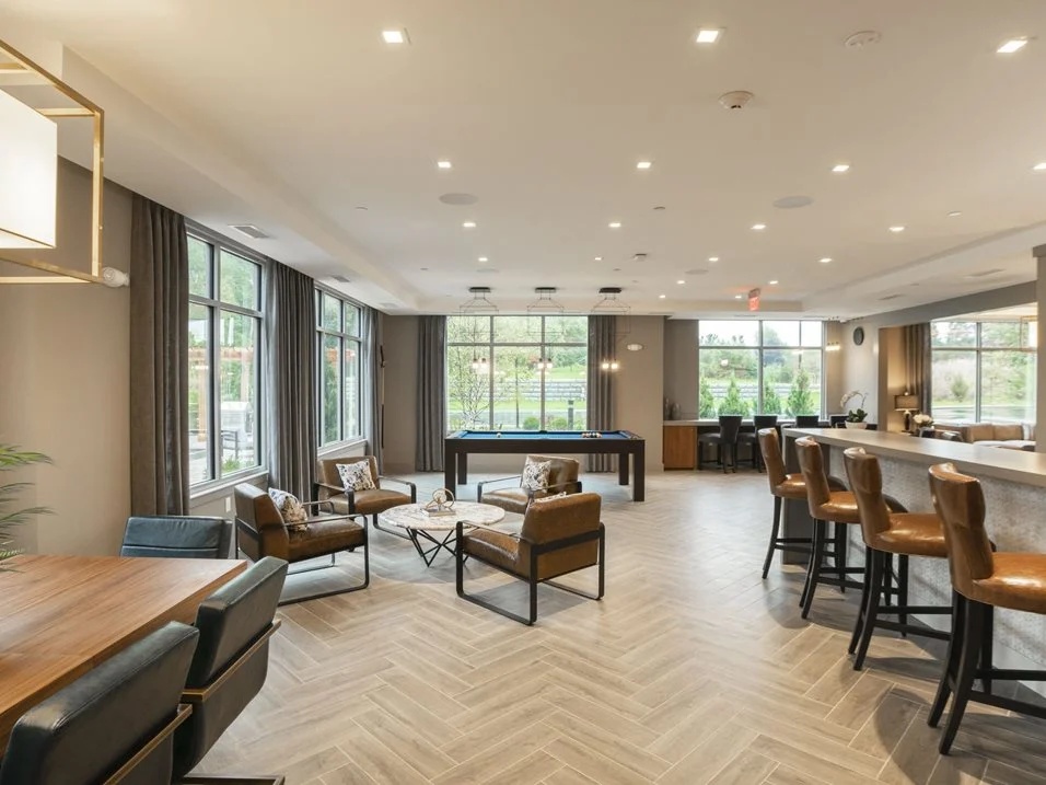 Resident lounge with chairs, tables, and large windows.