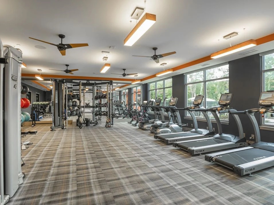 Fitness center with cardio machines and large windows.
