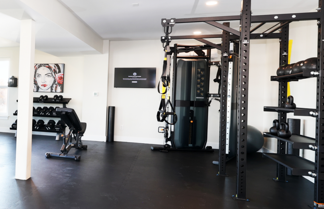 Fitness room with a strength-training rack, suspended exercise straps, and black flooring.